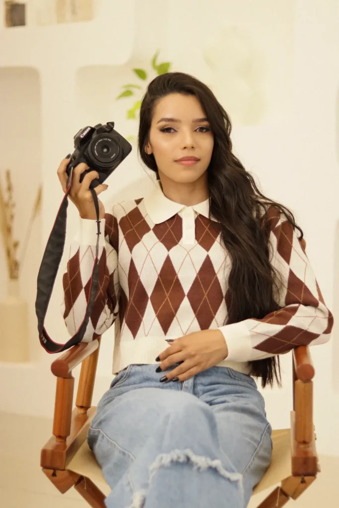 Fotógrafa Fernanda Santos sentada em cadeira de diretor, segurando câmera profissional, especializada em ensaios gestantes, femininos e corporativos em estúdio e locação externa